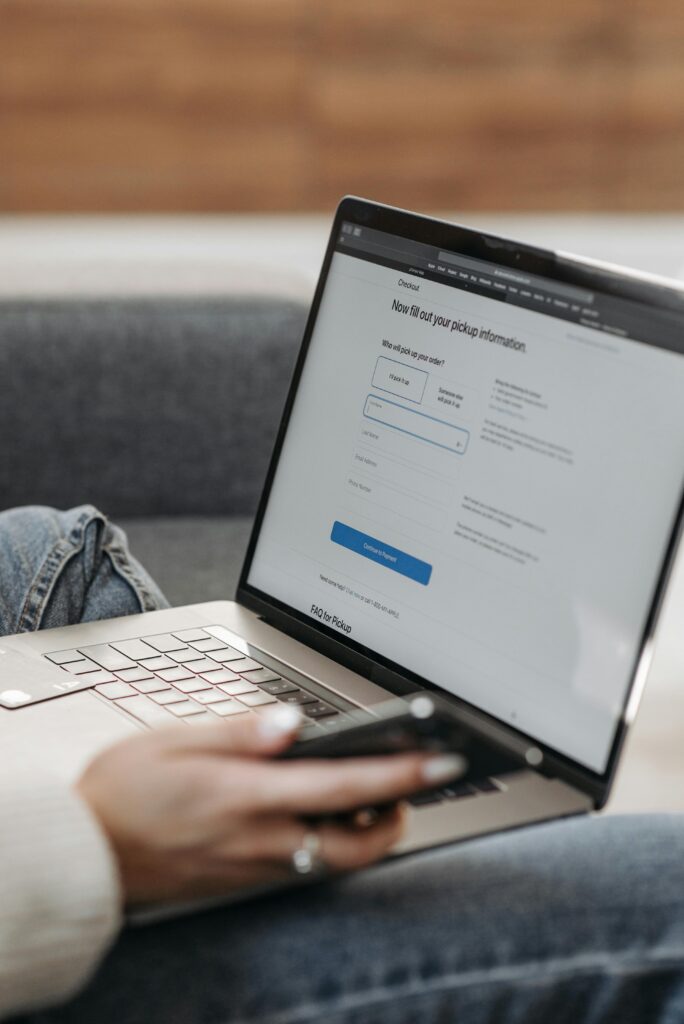 Close-up of a person using a laptop and smartphone indoors, focused on online task.